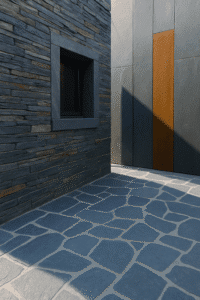 Stacked slate facade with framed window, opus incertum floor of irregular slates and rusty metal palisades in the background.